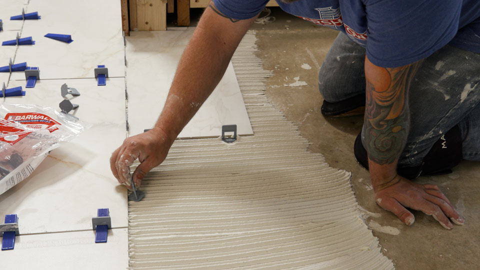 Person inserting spacer bases to floor tile during installation process.